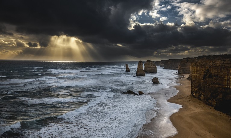 Sole che splende attraverso le nuvole sul mare. Scogliere sul lato destro e diverse rocce visibili tra le onde vicino alla riva