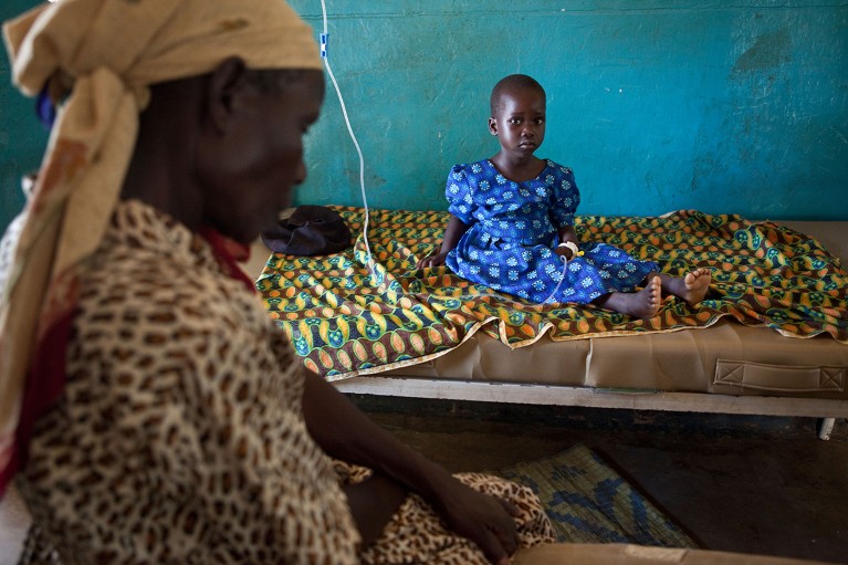 A young girl suffering from malaria sits in a hospital bed in Amuria, Uganda.