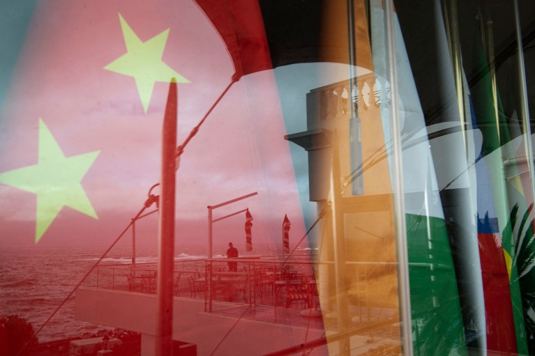 Close-up of a reflection on a window of a man staring at the sea in front of the national flags for China, India, Russia, South Africa and Brazil