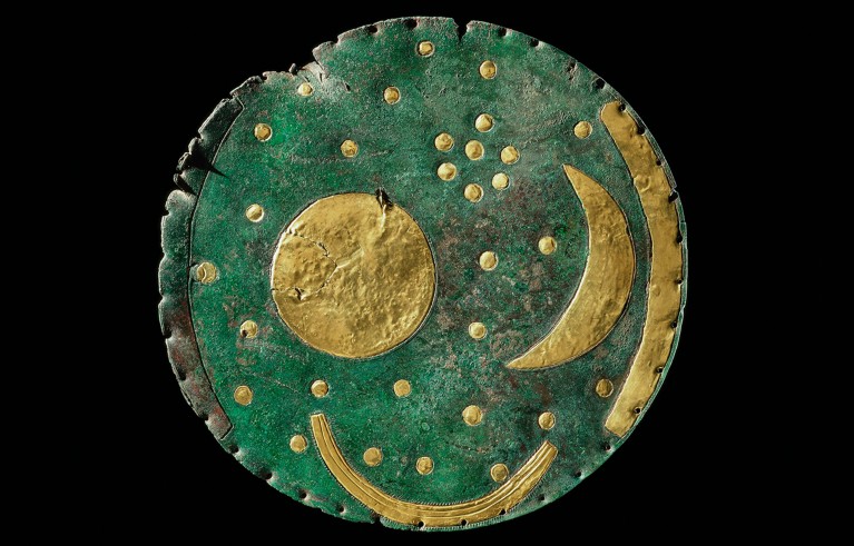 A green and gold metal disk featuring a design of a moon surrounded by stars, symbolising celestial themes.