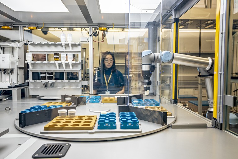 A photo showing Berkeley Lab researcher Yan Zeng looking at robot arm unloading a crucible filled with mixed powder precursors