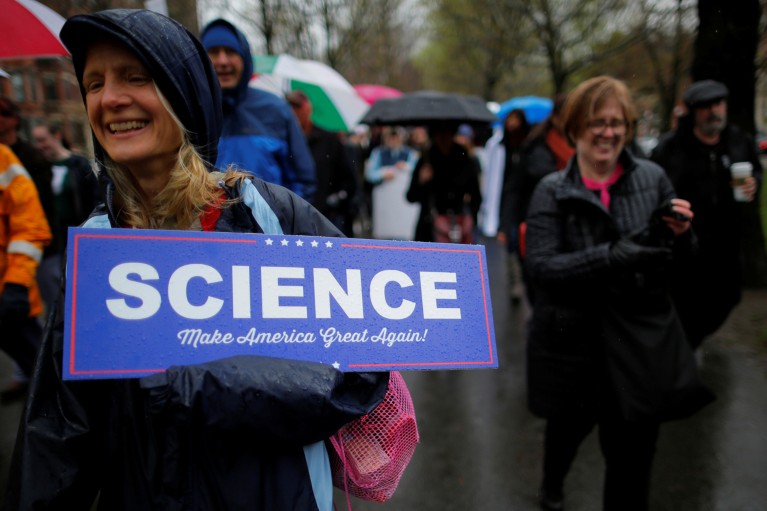 A woman carries a blue sign reading "Science" in the style of a campaign sign for U.S. President Donald Trump at a March for Science rally