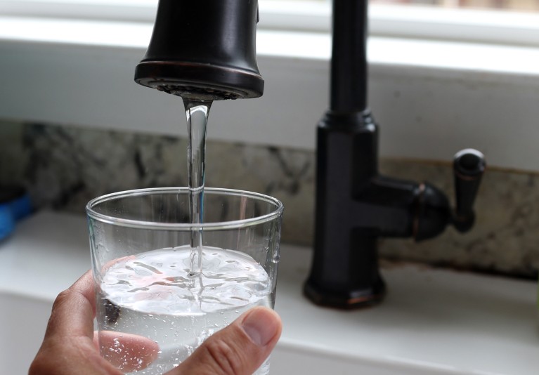 Close-up of a person holding a clear glass and filling it with water from a tap