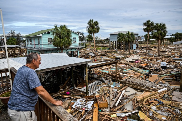 A man leans on a wooden barrier while looking at the damage done to his house after Hurricane Helene made landfall