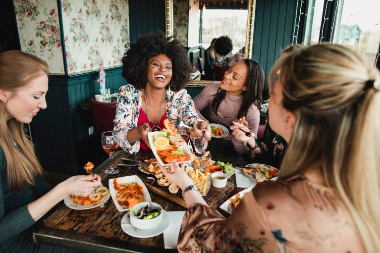 A group of women enjoy a meal and share food at a table in a restaurant.