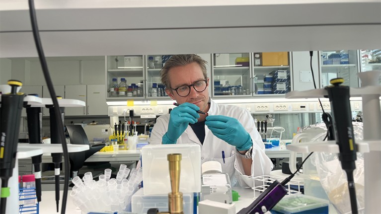 Laustsen-Kiel wearing glasses and a labcoat and surrounded by equipment marks a sample pot with a red pen