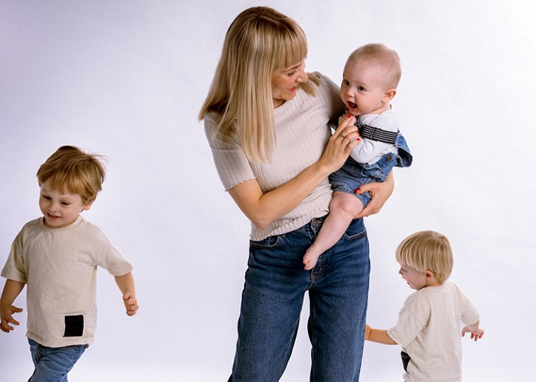 A photo of Cecilie Steenbuch Traberg holding her youngest child, while her other two children run past her