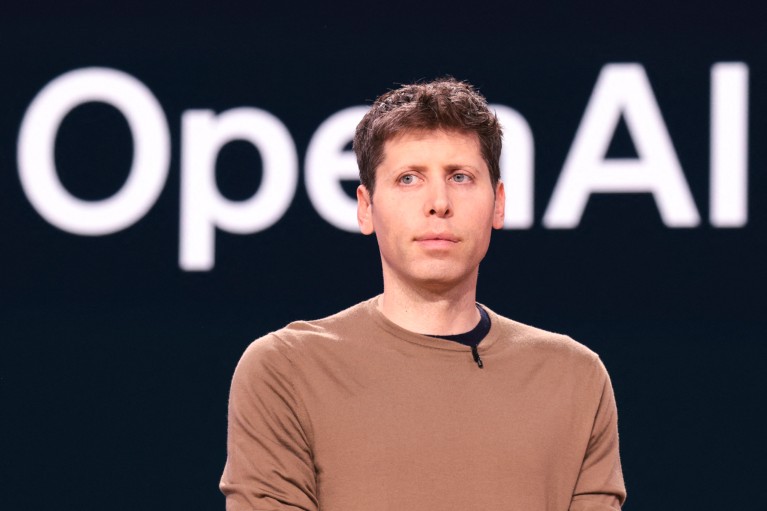 Close-up portrait of Sam Altman with a screen reading OpenAI behind him