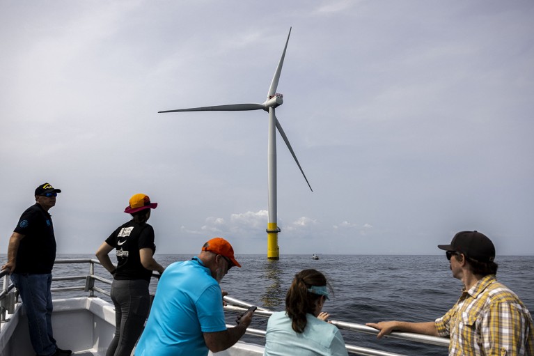 People on a ship look at a wind turbine located 27 miles off of Virginia Beach, U.S. in the Atlantic Ocean.