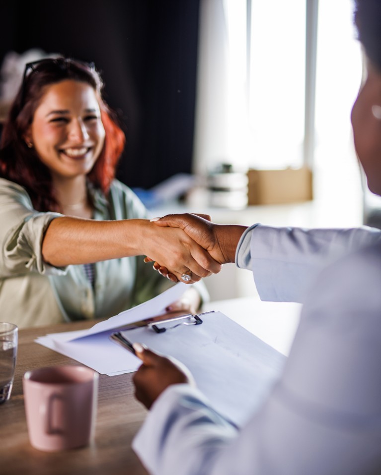 A job applicant shaking hands with a hiring manager over a desk during a job interview