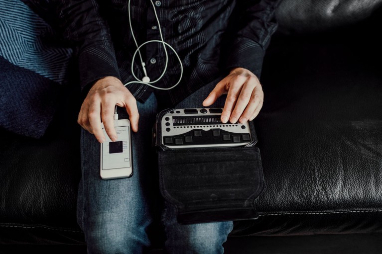 Hombre sentado en un sofá usando un teclado braille y un teléfono inteligente