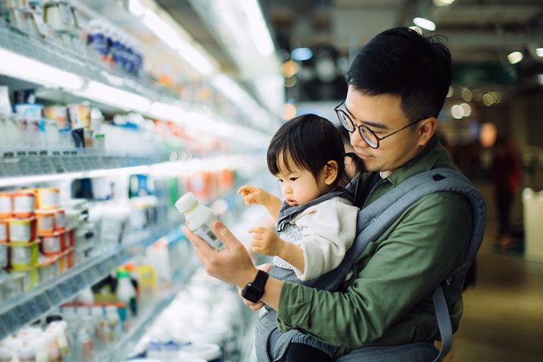 A man with a young toddler in a front babycarrier examine products in a supermarket