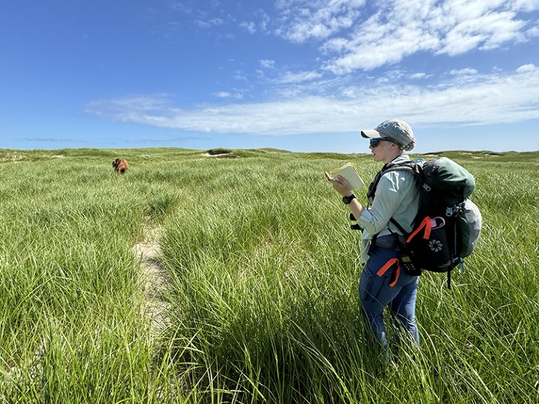 Victoria Crozier stands in long grass while holding a notebook