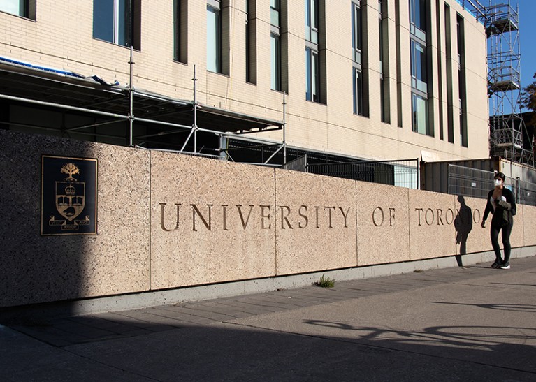 A student walks by an engraved stone sign for the University of Toronto