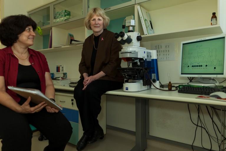 Mary-Claire King sitting on a lab bench next to a microscope and a computer