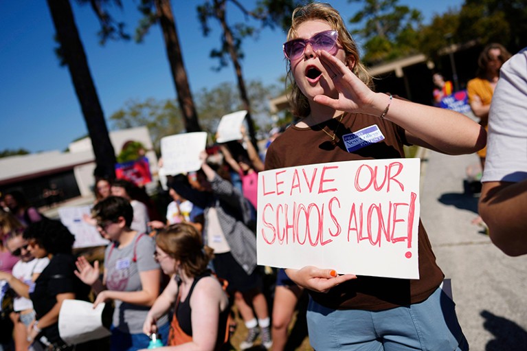 A woman shouts and holds a sign reading "Leave Our Schools Alone"