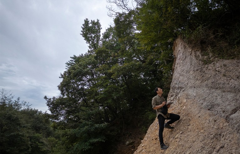 Geomorphologist Jeong-Sik Oh in equilibrium on a mountain slope holding a tablet to track hidden geographic markers on the surface to find places where active faults are likely to exist.