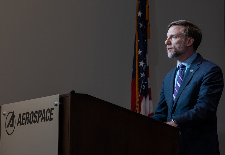 Jamie Morin stands behind a podium with the Aerospace logo on it.