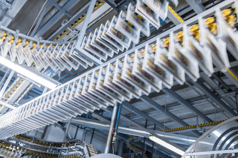 Blurred motion of newspapers moving along with overhead conveyor belt in modern printing press.