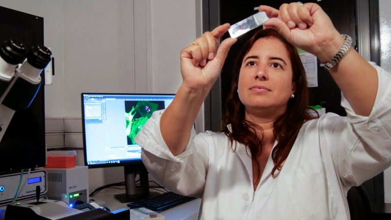 Marcela Díaz preparing a sample while sitting next to a microscope and computer monitor