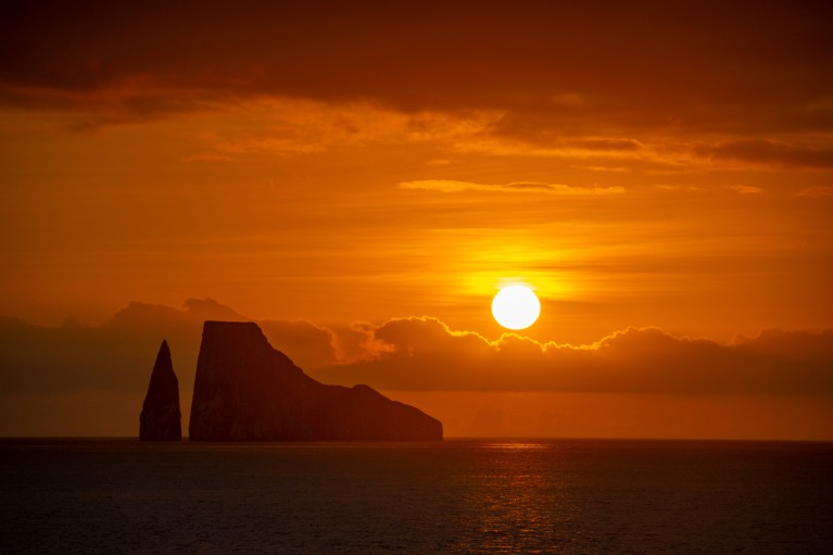 Il sole tramonta dietro due formazioni rocciose, illuminando il cielo di arancione