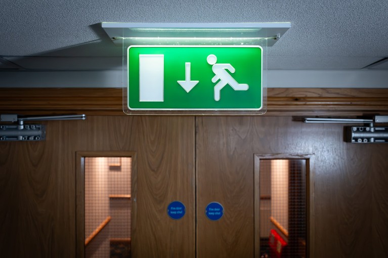 A green fire exit sign displayed above a pair of building interior fire doors.