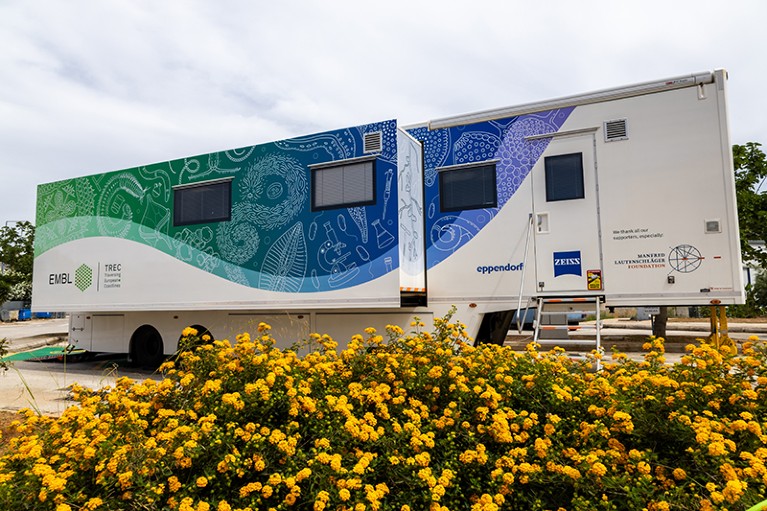 The The Advanced Mobile Laboratory is seen parked near a bed of yellow flowers