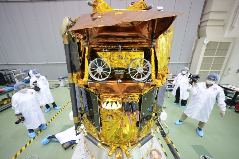 A gold-coloured lander carrying a rover in a laboratory, surrounded by staff in lab coats and face masks.