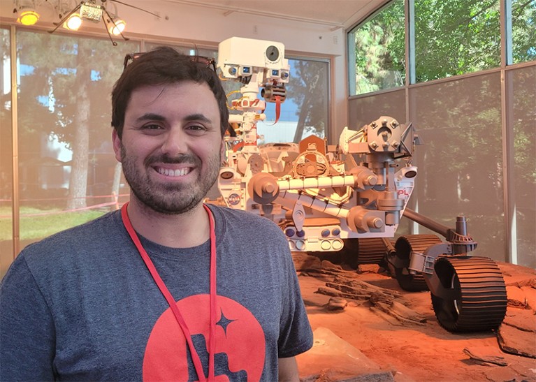 Nicolas Randazzo stands in front of a scale model of NASA's Perseverance rover.