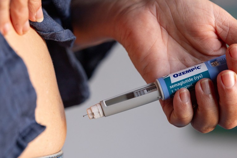 Close up view of a person holding an Ozempic needle injection pen close to their stomach.