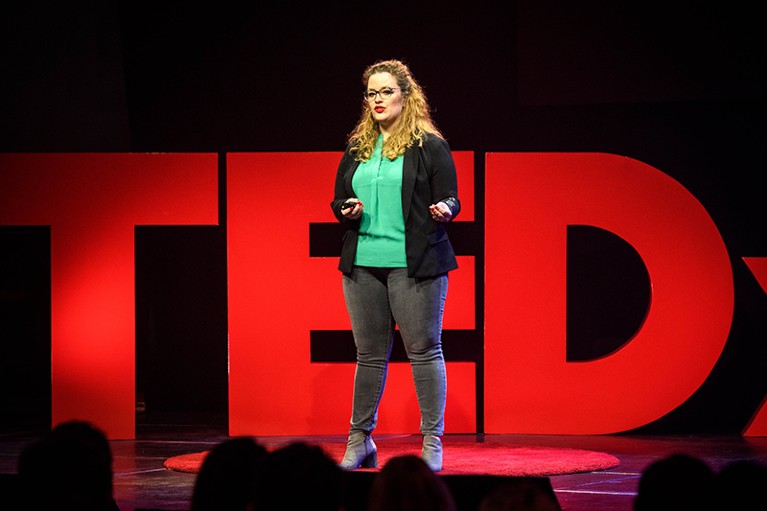 Laura Steenbergen stands on stage giving a talk at a TEDx event