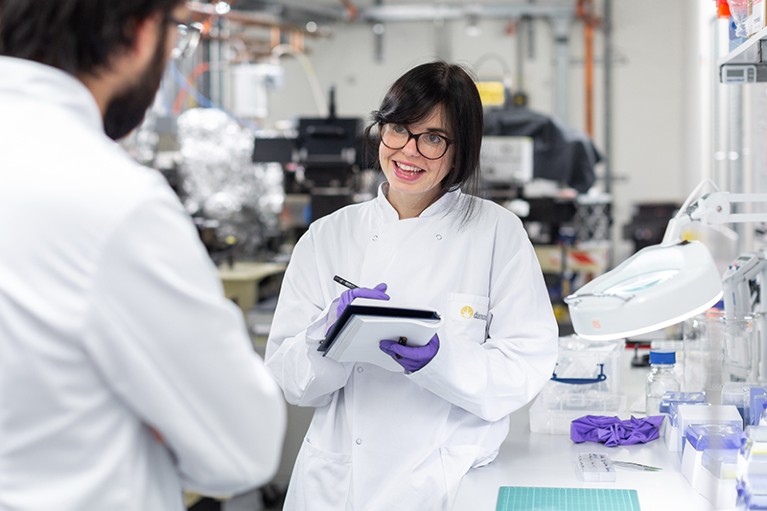 Jess is seen in a white lab coat and gloves in a lab at the Diamond Light Source