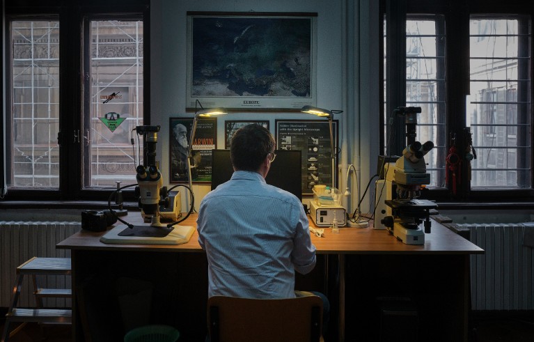 Mihai Emilian Popa sitting at a desk with a microscope and a desk lamp