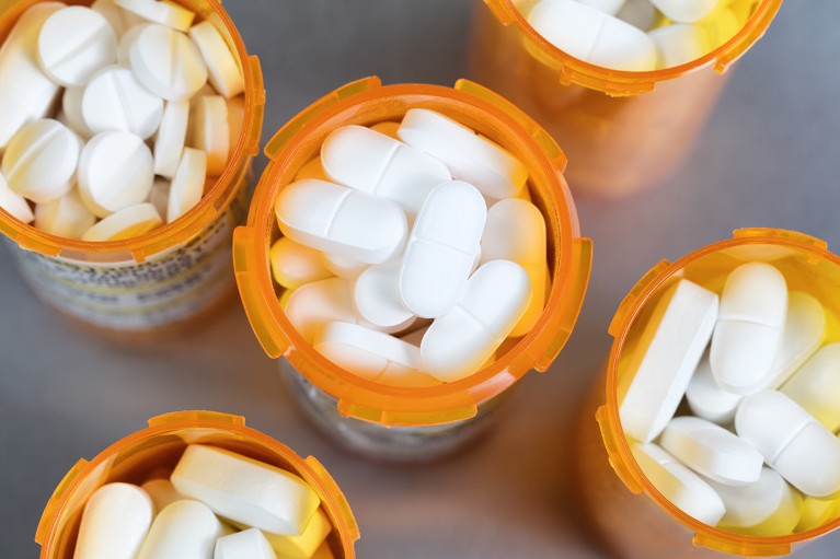 Close up overhead view of full prescription bottles of white tablets on a stainless steel background.