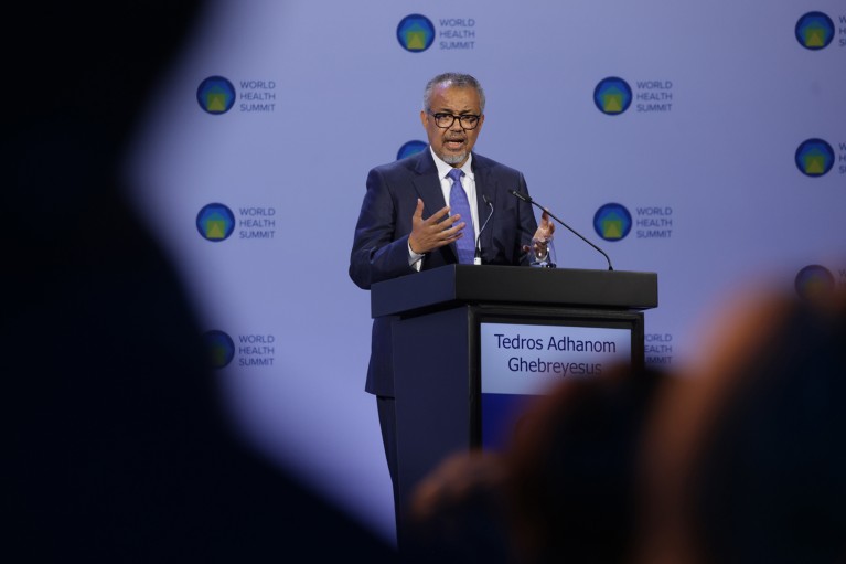 Tedros Adhanom Ghebreyesus stands at a lectern while giving a speech, gesturing with his hands