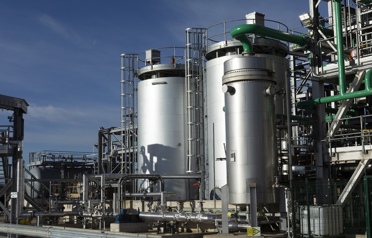 Exterior of Mura Technology plant. Two big metal cylinders are in the foreground and lots of pipes.