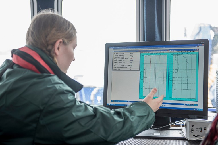 A female researchers gestures at water data displayed on a computer screen onboard a research ship.