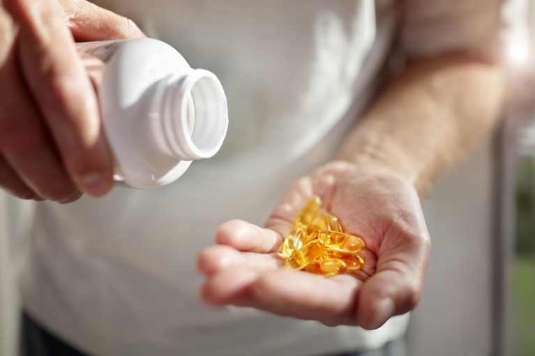 Close up on the hands of a senior man holding a white bottle and a handful of yellow omega-3 supplement capsules