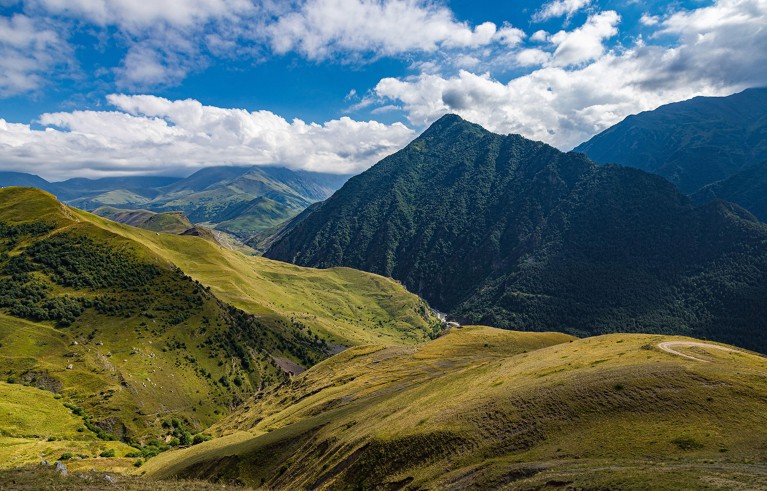 An expansive view of the green hills and tall peaks of the Caucasus mountains.