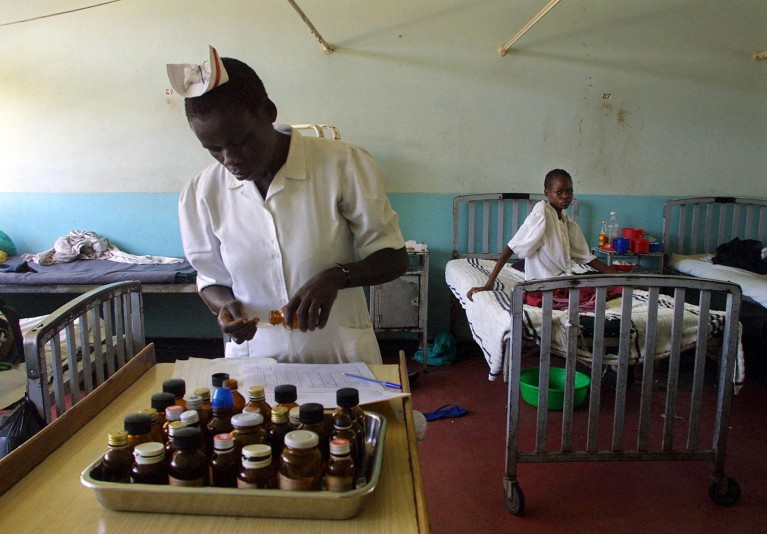 A Kenyan nurse measures out doses of medicine intended for AIDS patients at the Homa Bay Hospital, western Kenya while a patient in bed looks on.