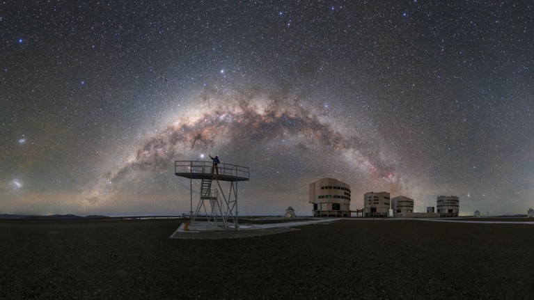 The Milky Way arcs above ESO’s Paranal Observatory, while a person points upwards