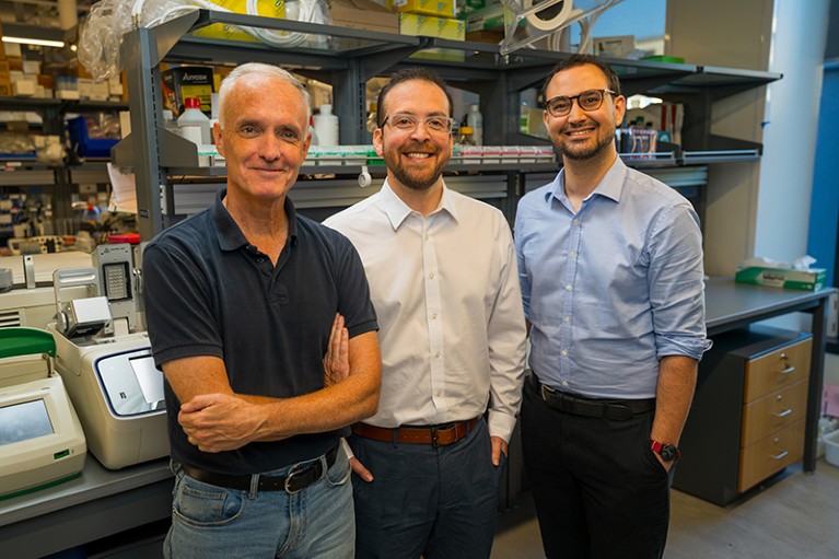 Three smiling men stand next to each other in a laboratory