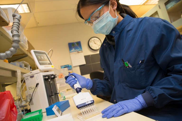 Close-up of a young female scientist wearing a face mask and eye goggles, working in the lab