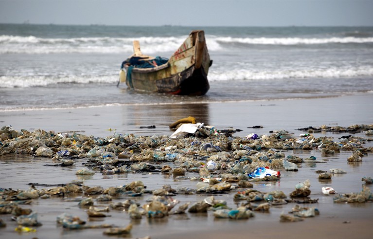 Plastic bottles, litter, bags and other waste that has been washed up from the sea litters the beach in front of a fishing boat in Accra, Ghana.