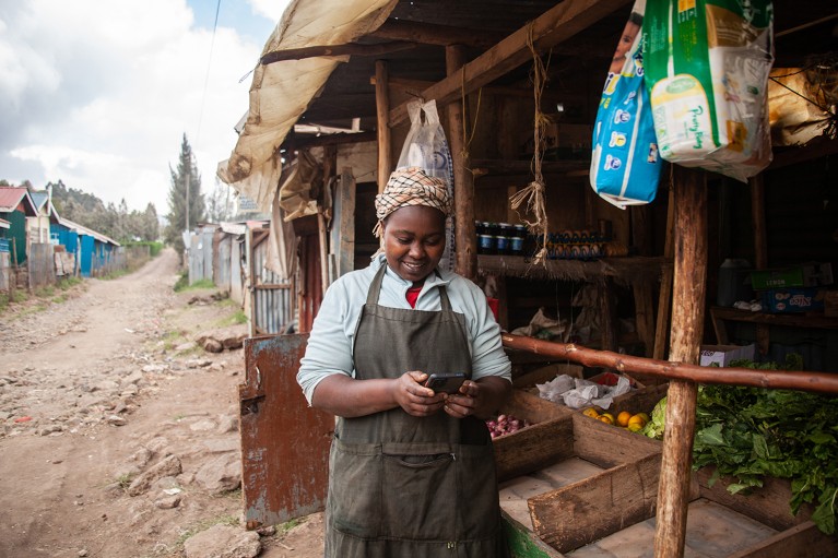 Una donna usa il suo telefono per vedere i recenti pagamenti dei clienti nella sua bancarella di generi alimentari a Kajiado, in Kenya.