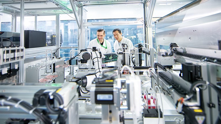 Two males peer into a room filled with scientific equipment.