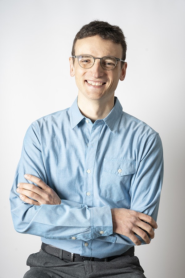 White male wearing glasses and a blue shirt is smiling to camera.