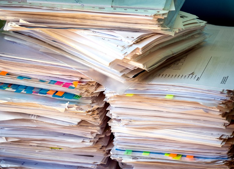 A large stack of papers and folders with coloured tabs.