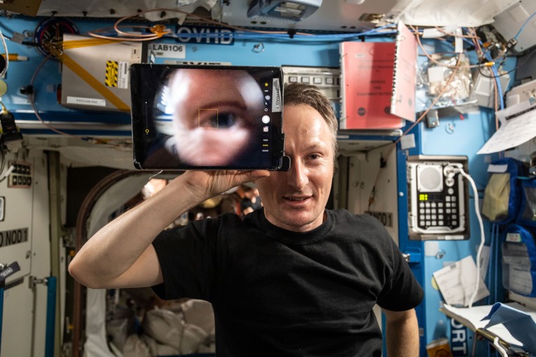 Portrait of an astronaut using an opthalmic lens attached to a tablet showing a close-up of his eye on the ISS