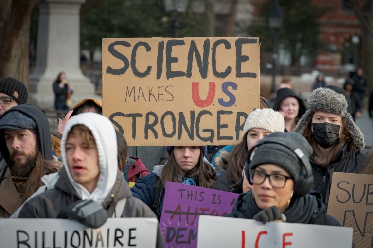 Someone holds a brown sign within a group of protesters reading "Science makes U.S. stronger"